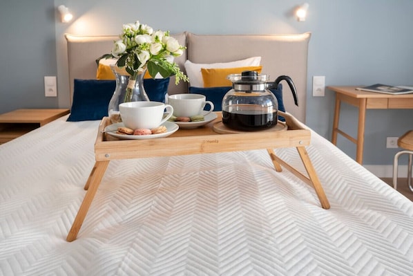 A neatly made bed with a wooden tray holding a coffee pot, cups, and a vase of flowers.