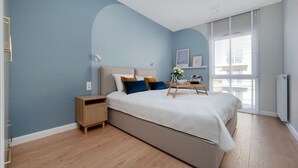 Een slaapkamer met een bed, nachtkastje en een raam met zonwering.