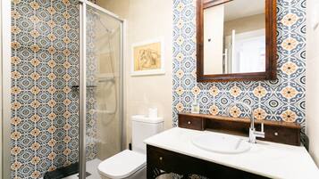 Une salle de bain avec des carreaux décoratifs, une douche en verre, des toilettes, un lavabo avec un miroir et une œuvre d’art encadrée au mur.