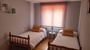 A room with two wooden beds, a small table, and a window with blinds. - Atico con Terraza en Vilagarcia de Arousa (Vilagarcia de Arousa)