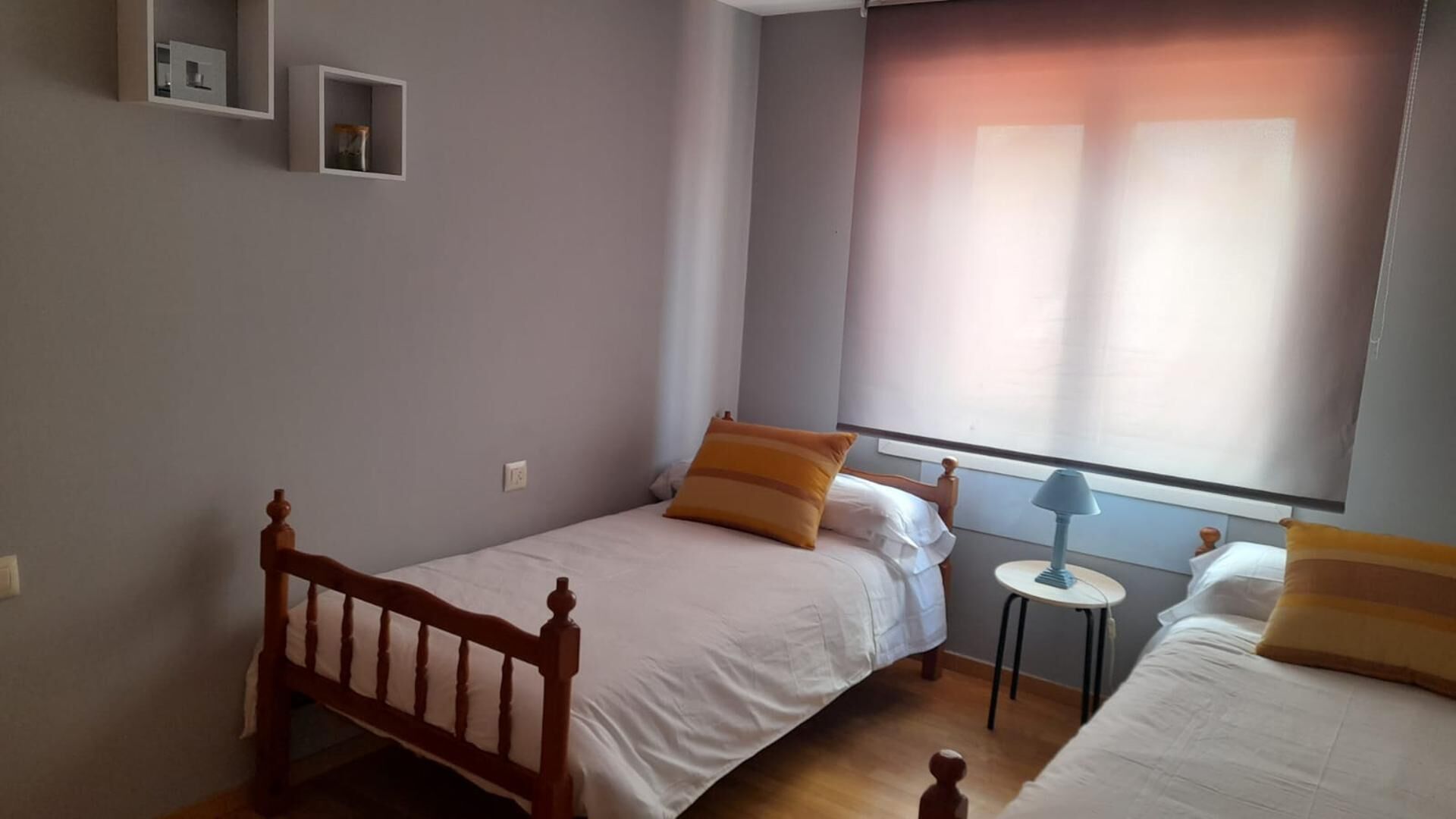 A small, neatly arranged bedroom with a single bed, a bedside table, and a window with curtains.