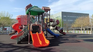 A playground with multiple slides and climbing structures, surrounded by a fenced area and trees. - 3 Bed Flat - Sleeps 6 - Pool - Garden - Parking (Vilagarcia de Arousa)