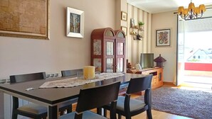 A dining area with a long table, chairs, a chandelier, and a view of the outside. - 3 Bed Flat - Sleeps 6 - Pool - Garden - Parking (Vilagarcia de Arousa)