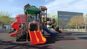 A playground with multiple slides and climbing structures, surrounded by a fenced area and trees. - Piso Para 6 Personas con Garaje Gratuito (Vilagarcia de Arousa)