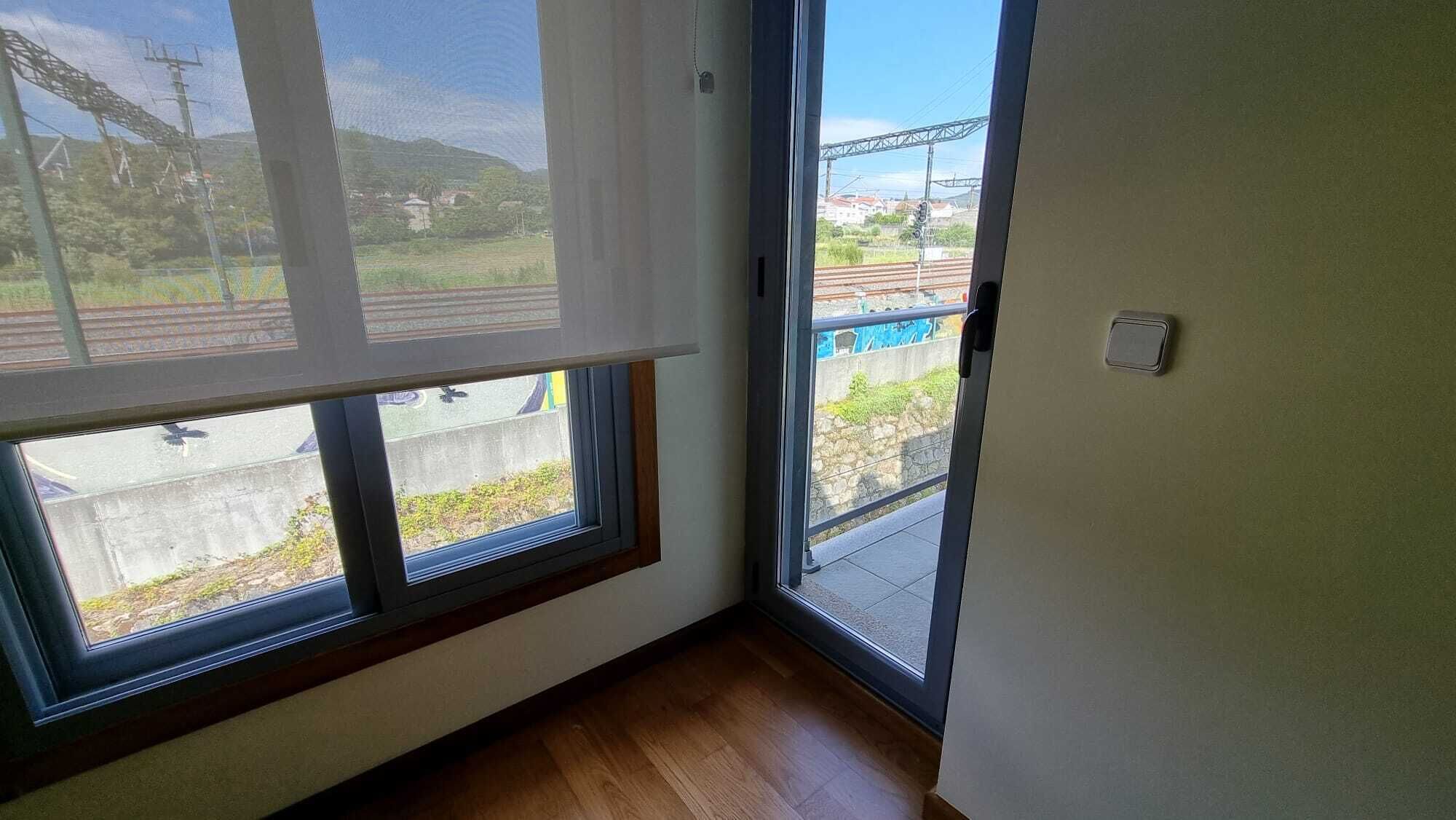Une pièce dotée de grandes fenêtres donnant sur une voie ferrée et sur un paysage verdoyant.