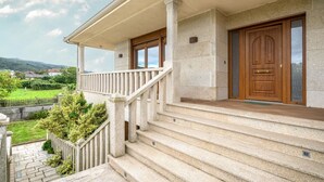 A stone staircase leading to a wooden door with a glass panel, a covered porch, and a view of a green landscape. - Casa de Lujo con Pisicina y Jardin en el Rural (Meis)