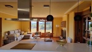 A modern living room with a sofa, coffee table, and a large island with a bowl. There is a view of greenery outside through large windows. - Casa de Lujo con Pisicina y Jardin en el Rural (Meis)