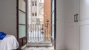 A room with a bed, a patterned floor, and a view of a historic building through an open door. - Primis - CatedralHomes (Avila)