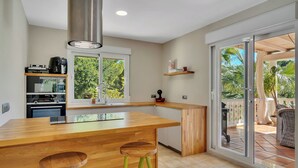 Una cocina moderna con una isla de madera, taburetes verdes y vistas al exterior a través de amplias puertas correderas de vidrio.