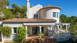 Una casa de dos pisos con piscina, un porche cubierto y un jardín.