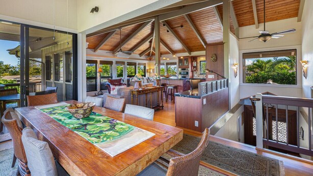 Un vaste espace de vie à aire ouverte comprenant une salle à manger avec une table en bois, des sièges confortables, une cuisine et une vue sur la verdure.
