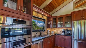 Une cuisine moderne dotée d’appareils électroménagers en acier inoxydable, de meubles en bois et d’une grande fenêtre donnant sur un jardin.