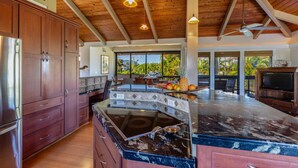 Une cuisine spacieuse avec des meubles en bois, un grand îlot central et une vue sur un paysage tropical.