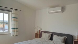 A bedroom with a bed, a window with curtains, a bedside table with a lamp, and an air conditioning unit on the wall. - Herdade do Castanheiro nur Wenige Min. von Lagos in Traumhafter Ruhiger Lage (Bensafrim/ Lagos)