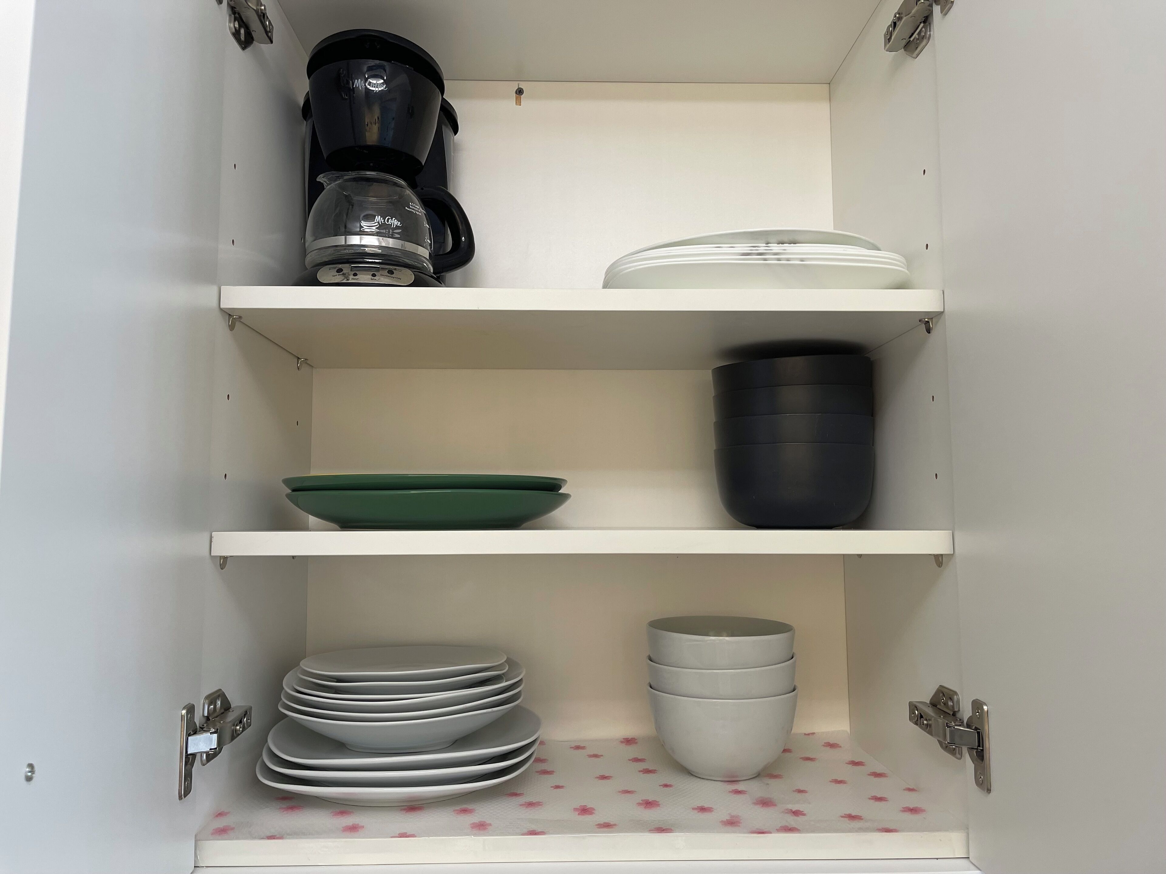 Ein Küchenschrank mit Regalen, der verschiedene Küchenutensilien beherbergt, darunter eine Kaffeemaschine, Teller, Schüsseln und Tassen.