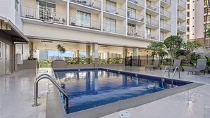A swimming pool with a metal railing, surrounded by lounge chairs and potted plants, with a multi-story building in the background. - Charming cozy condo in marvelous Honolulu with WiFi (Honolulu)
