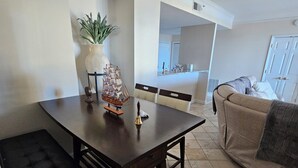 A dining area with a dark wooden table, black cushioned chairs, and a ship model centerpiece. A potted plant is on the wall, and a beige sofa is in the background. - Luxury 2-bedroom waterfront condo with parking, in sunny South Tampa (Tampa)