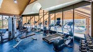 Ein Fitnessstudio mit verschiedenen Trainingsgeräten, großen Fenstern und einer hohen Decke.