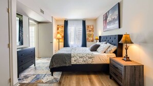 Ein Schlafzimmer mit einem Bett, Nachttischen, einem Schminktisch und einem Fenster mit Vorhängen.