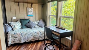 Een gezellige slaapkamer met een bed, een bureau en een raam met uitzicht op groen.