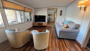 Een woonkamer met een televisie, rieten meubels, een grijze bank en een houten vloer.