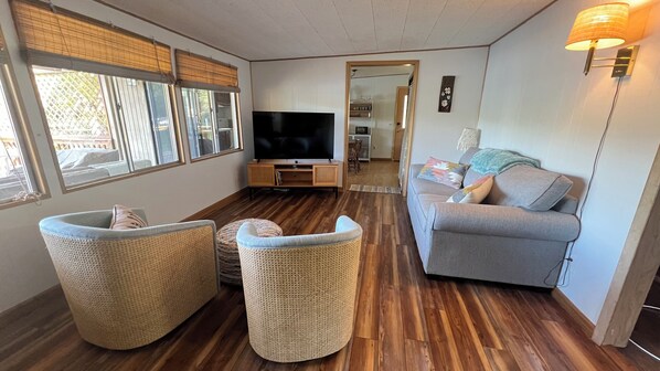 A living room with a TV, wicker furniture, a grey sofa, and a wooden floor.