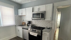 A kitchen with white cabinets, a stainless steel stove, a microwave, and a tiled backsplash.
