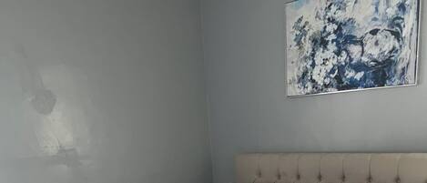 A neatly made bed with white linens and rolled towels, a tufted headboard, and a painting on the wall.