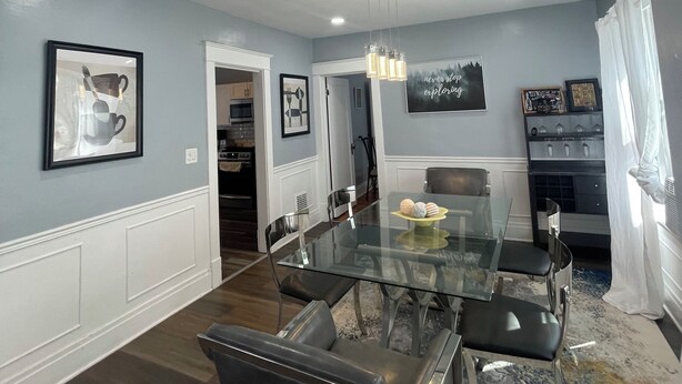 A modern dining room with a glass table, black chairs, and a chandelier.