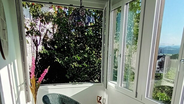 A sunlit patio with two wicker chairs and a small table, a vase with flowers, and a hanging light fixture.