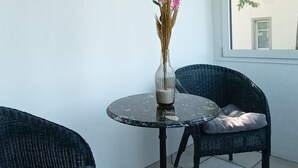 A patio with two wicker chairs, a round table with a vase of flowers, a decorative clock, and a stained glass window.