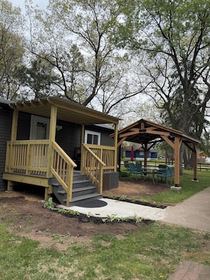 A wooden building with a porch and stairs, a covered patio area, and a small garden with plants.
