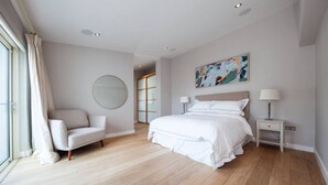 Een moderne slaapkamer met een groot bed, een bank, een nachtkastje en een spiegel.