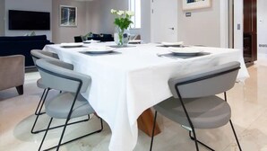 Een moderne eethoek met een witte tafel, grijze stoelen en een bloemetjesvaas.