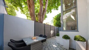 Een terras met een tafel, stoelen, een vuurplaats, vloer met een patroon en potplanten.