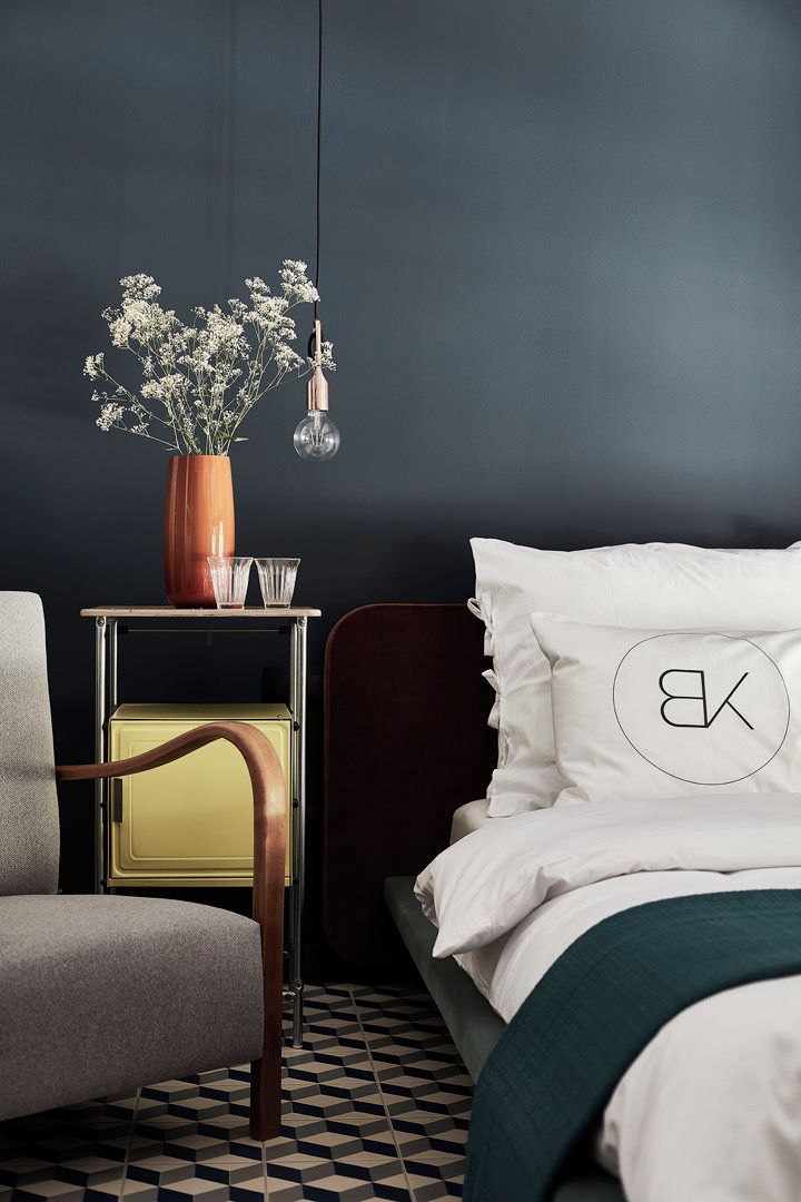 A bedroom with a bed, a chair, a nightstand, a vase with flowers, and a hanging light.