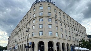 Un edificio grande y curvo con el nombre "Mercedes-Benz" en la parte superior. Tiene varios pisos con numerosas ventanas y una serie de arcos a nivel de calle.