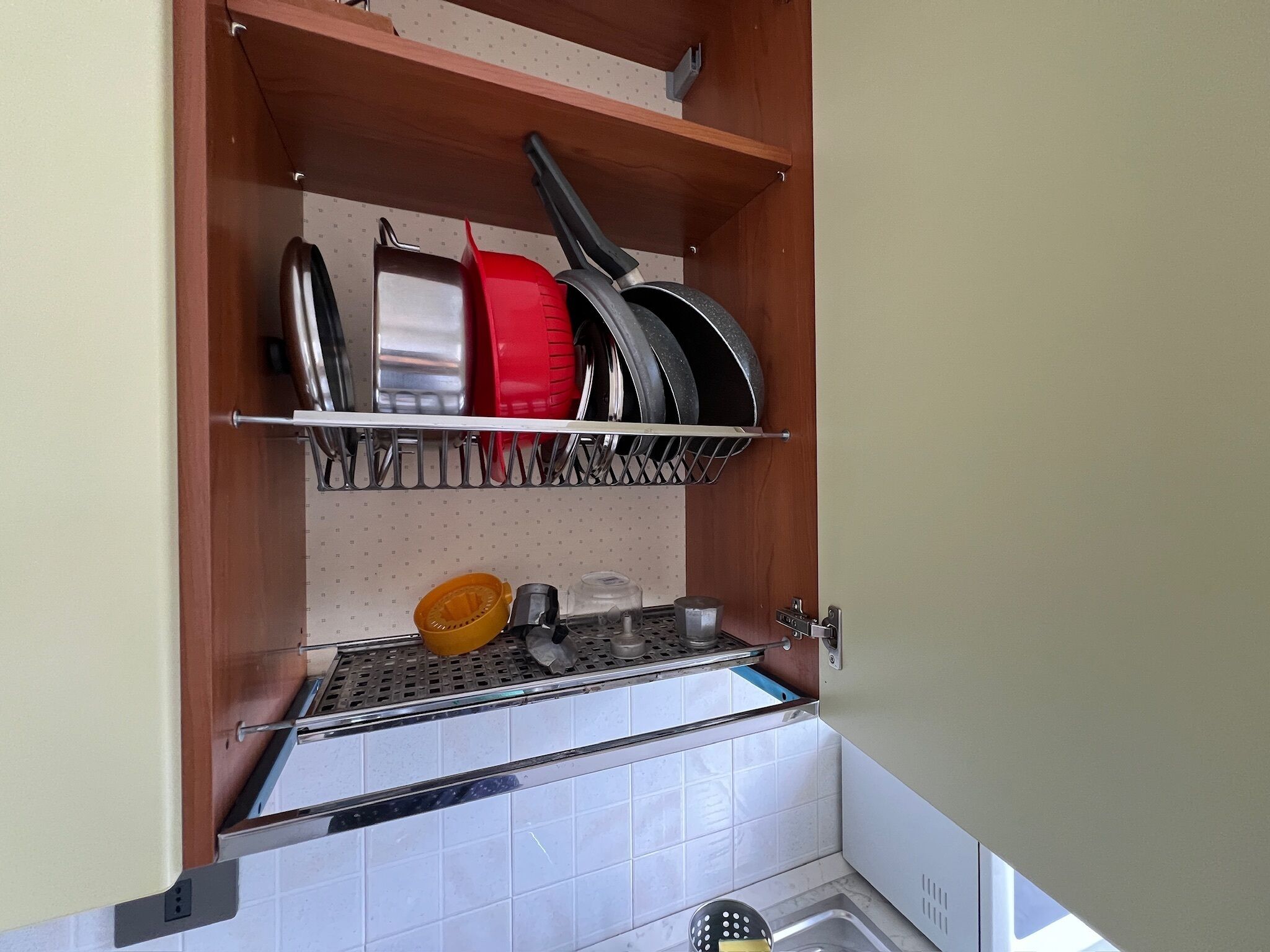 Una cocina con una estantería metálica que sostiene ollas y sartenes, un fregadero y un salpicadero de azulejos.