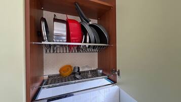 Una cocina con una estantería metálica que sostiene ollas y sartenes, un fregadero y un salpicadero de azulejos.