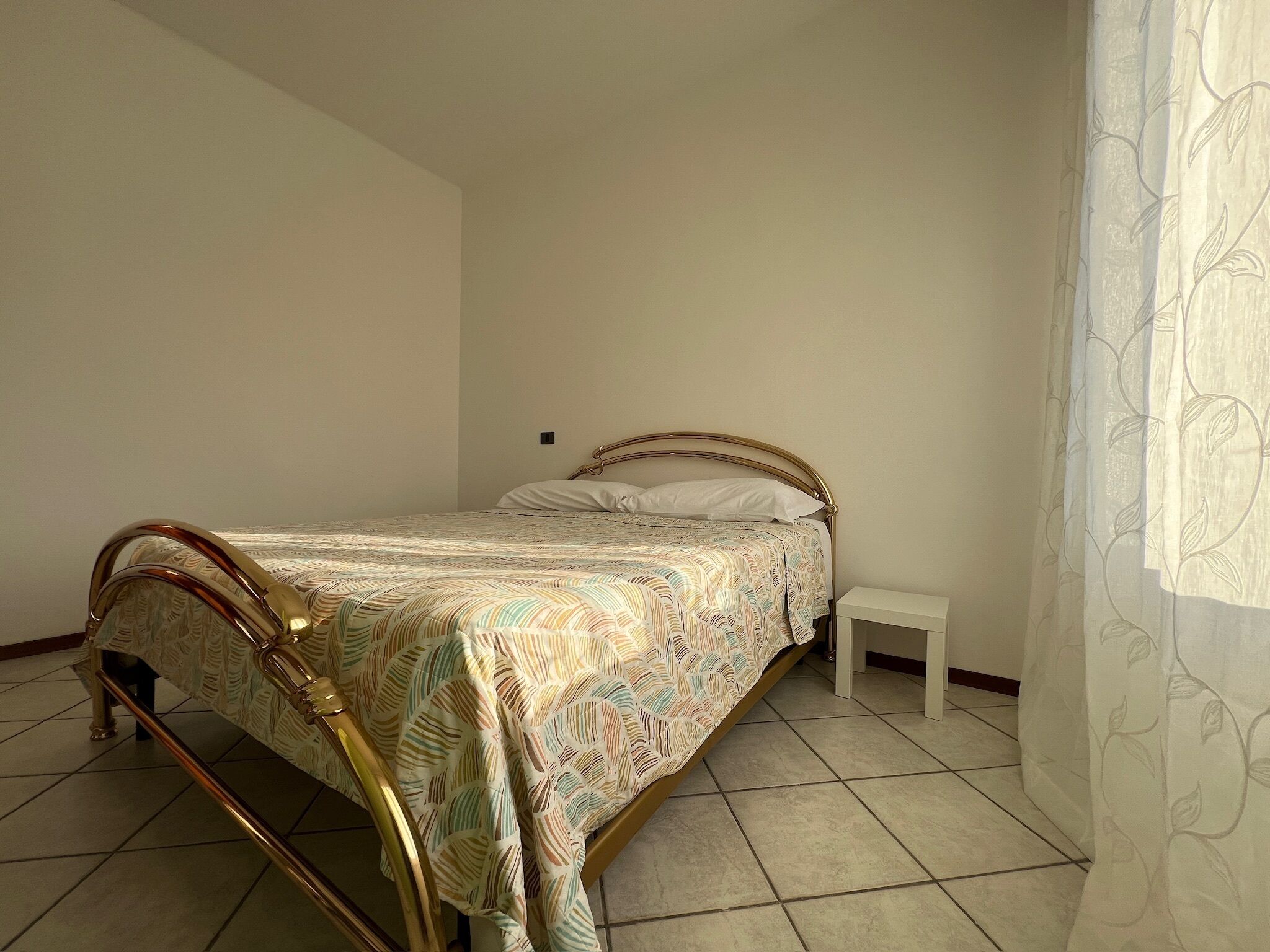 A single bed with a patterned bedspread, a small bedside table, and a curtain with a leaf pattern.