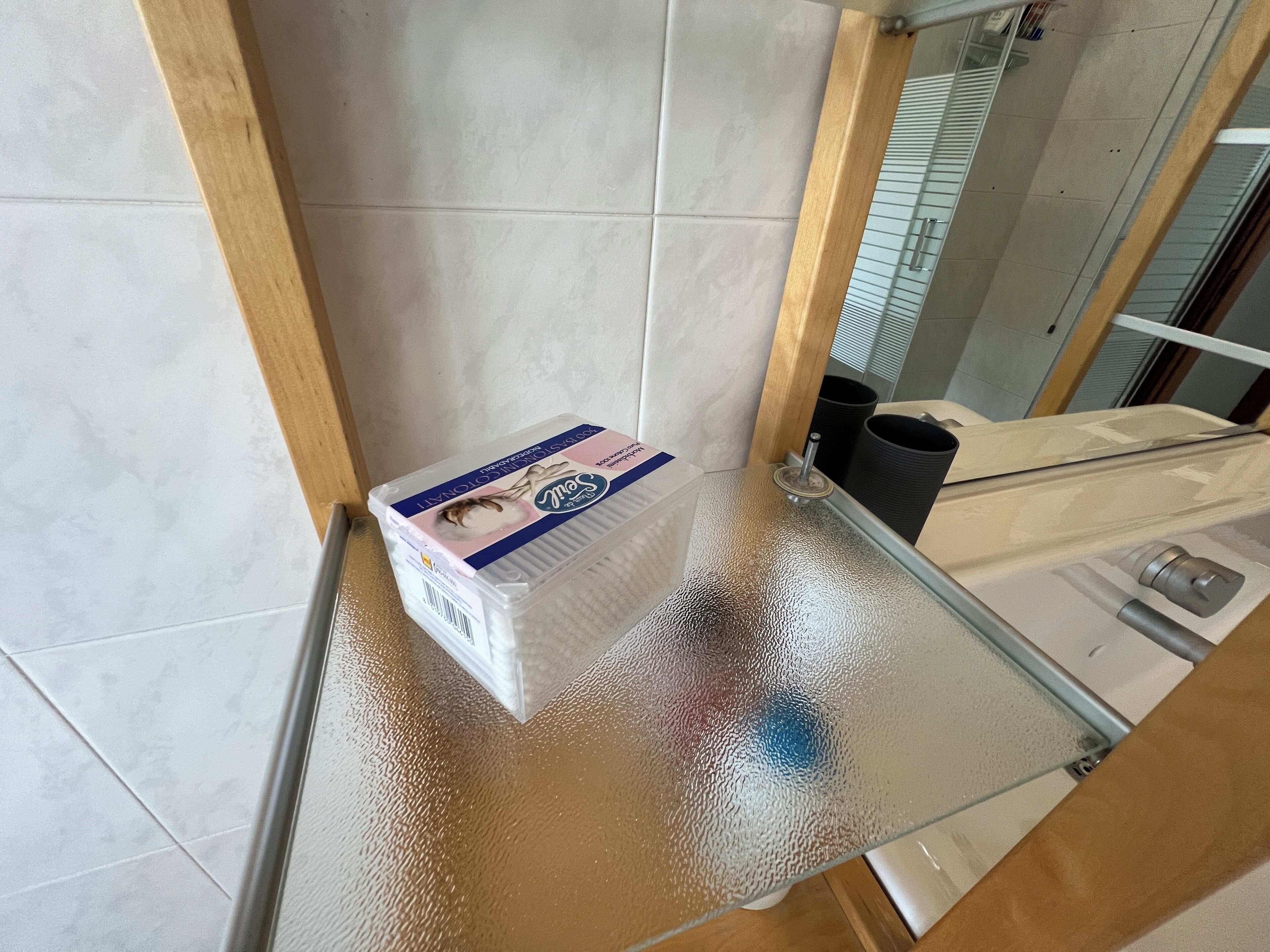 A bathroom with a glass shower enclosure, a white toilet, and a trash bin.