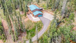 Una casa grande de dos pisos con techo azul, rodeada de un bosque frondoso.