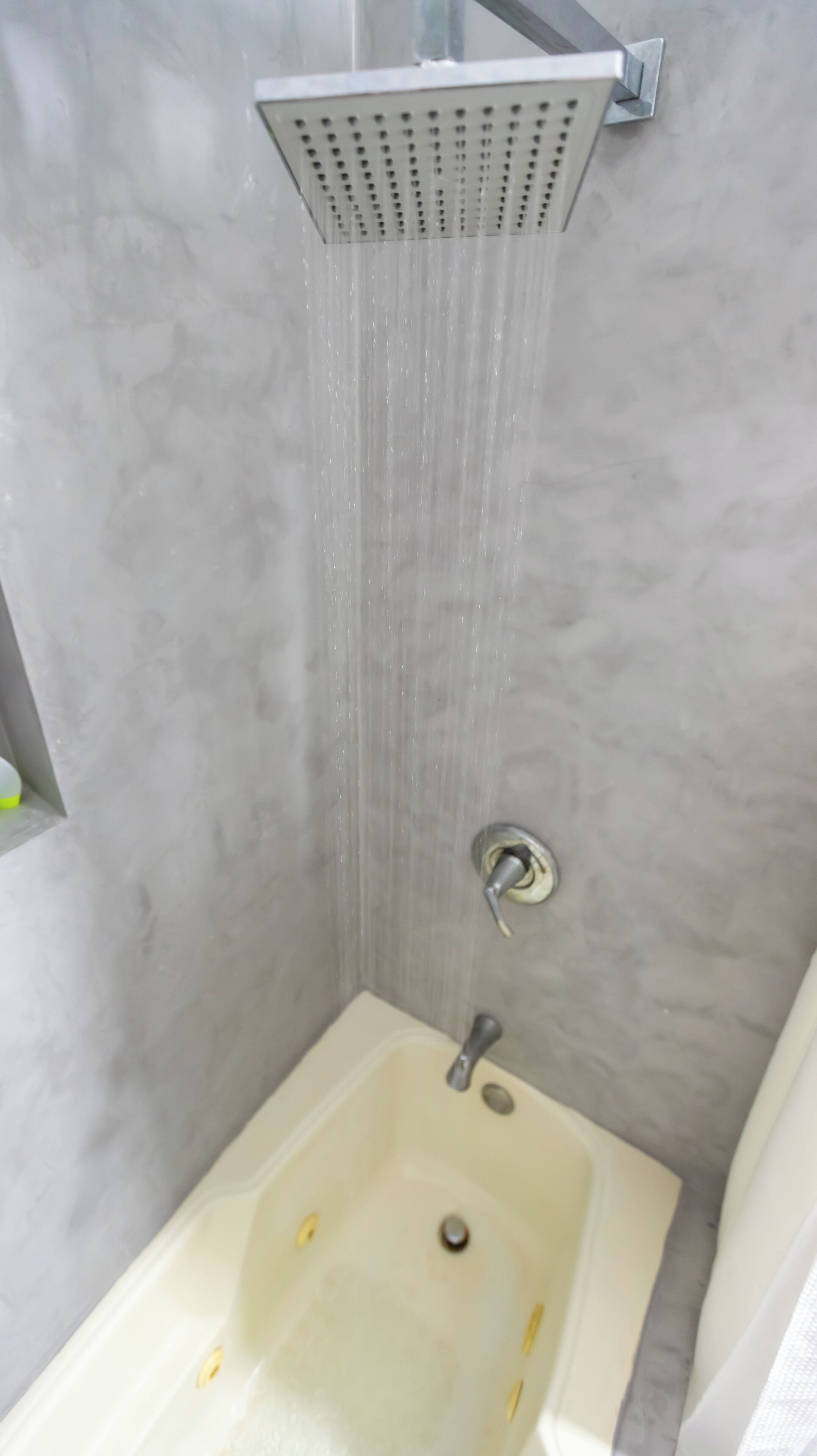 Eine Dusche mit einer quadratischen, beigen Badewanne und einer an der Wand befestigten Duschbrause.
