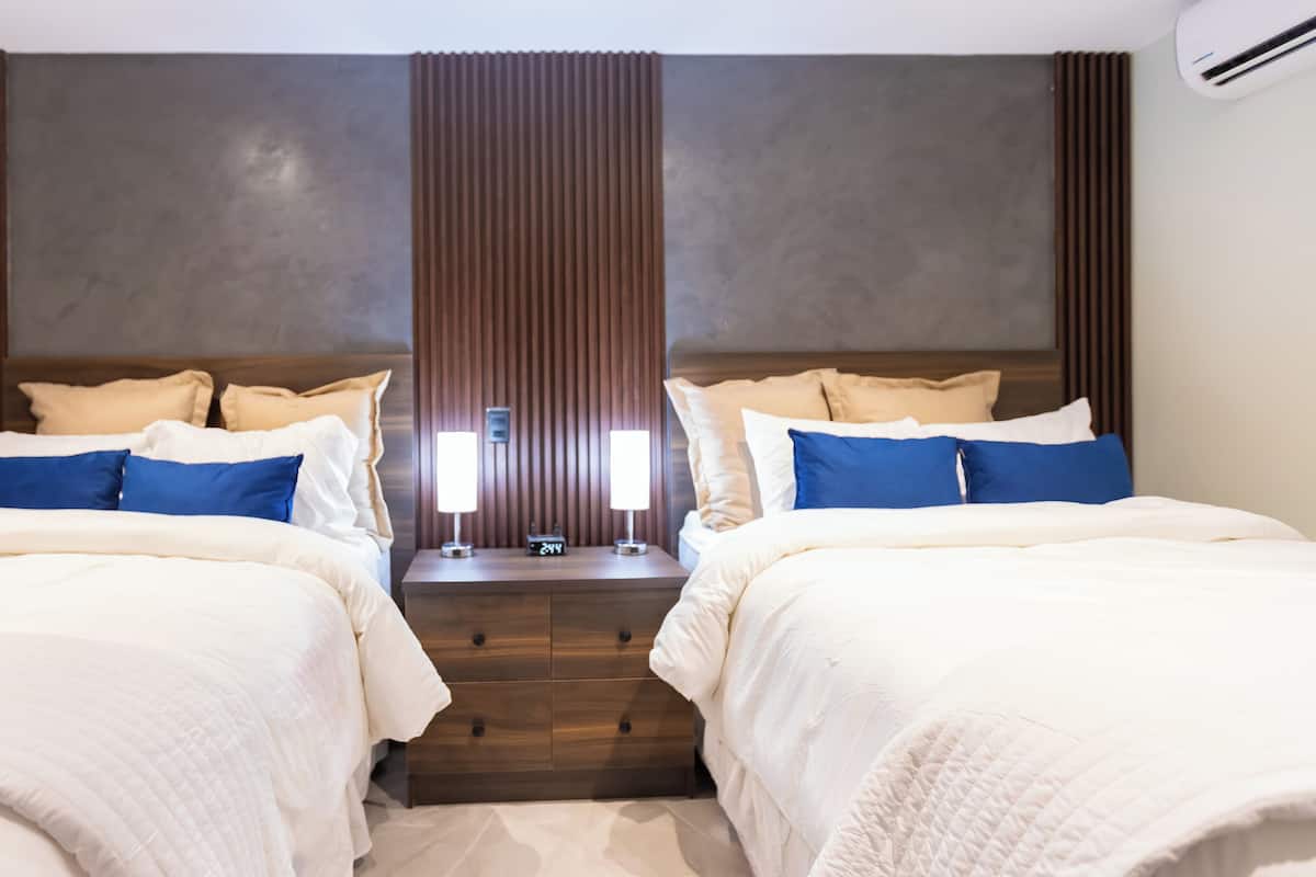 A hotel room with two beds, a wooden headboard, bedside lamps, and a digital clock.