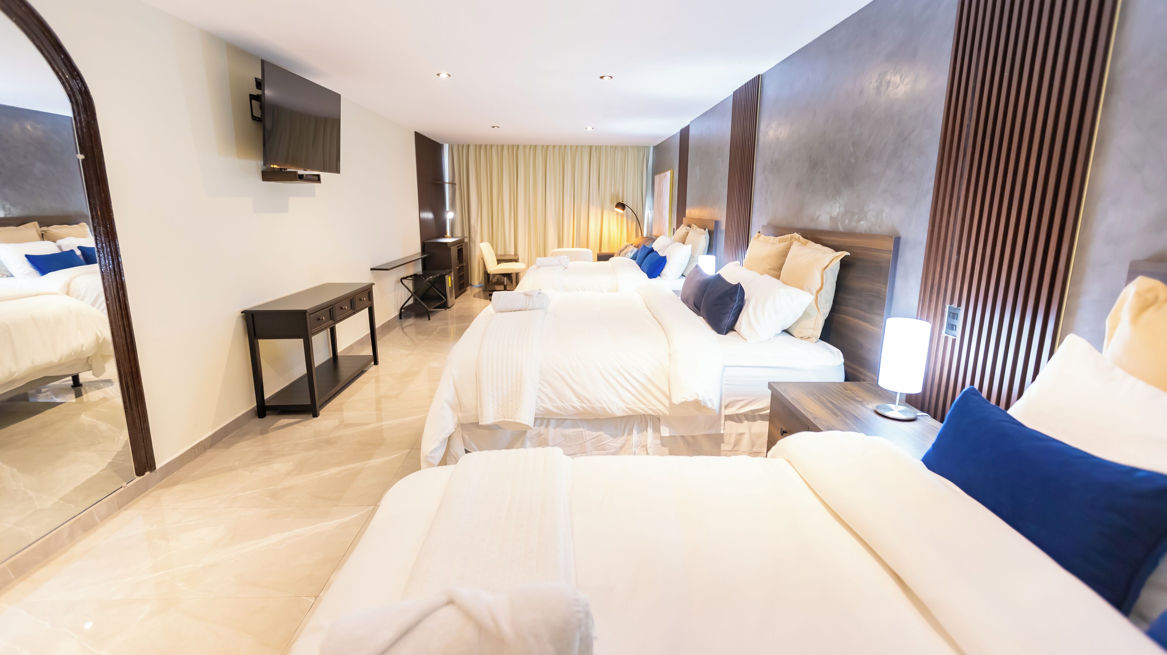 A hotel room with three beds, a TV mounted on the wall, a desk, and a chair.