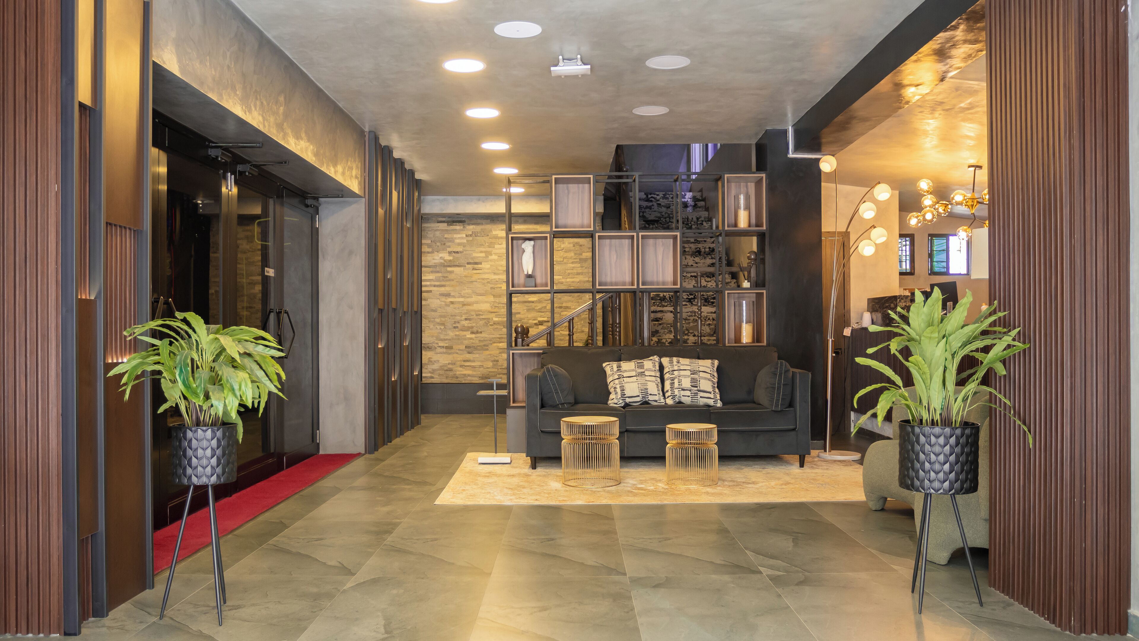 A modern lobby with a dark sofa, a red carpet, and potted plants.