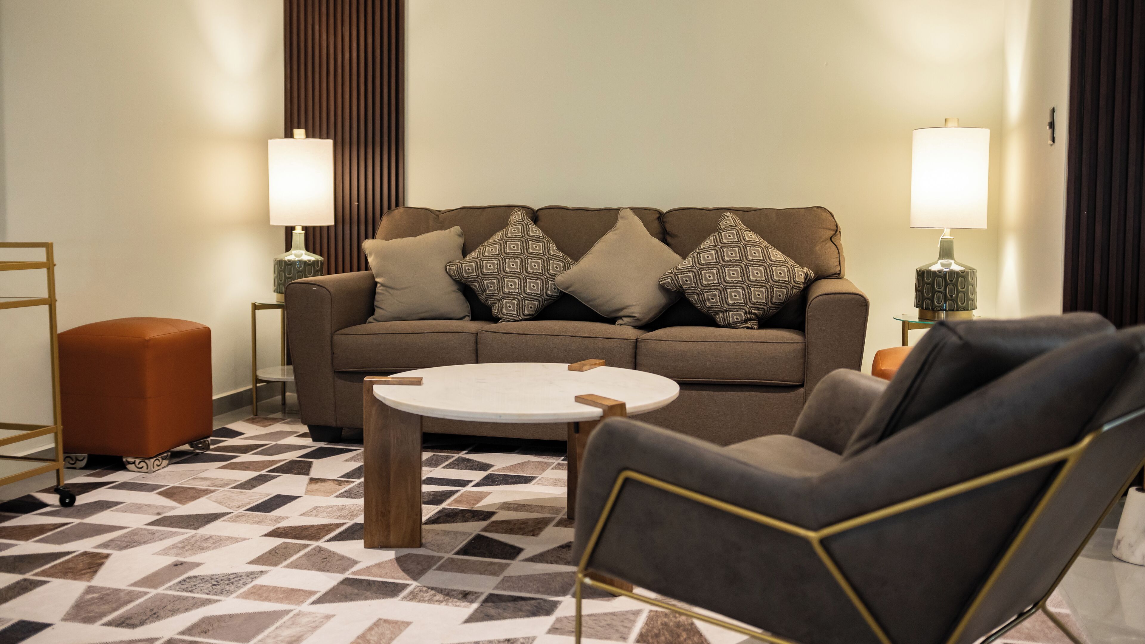 A modern living room with a sofa, armchair, ottoman, and a round coffee table.