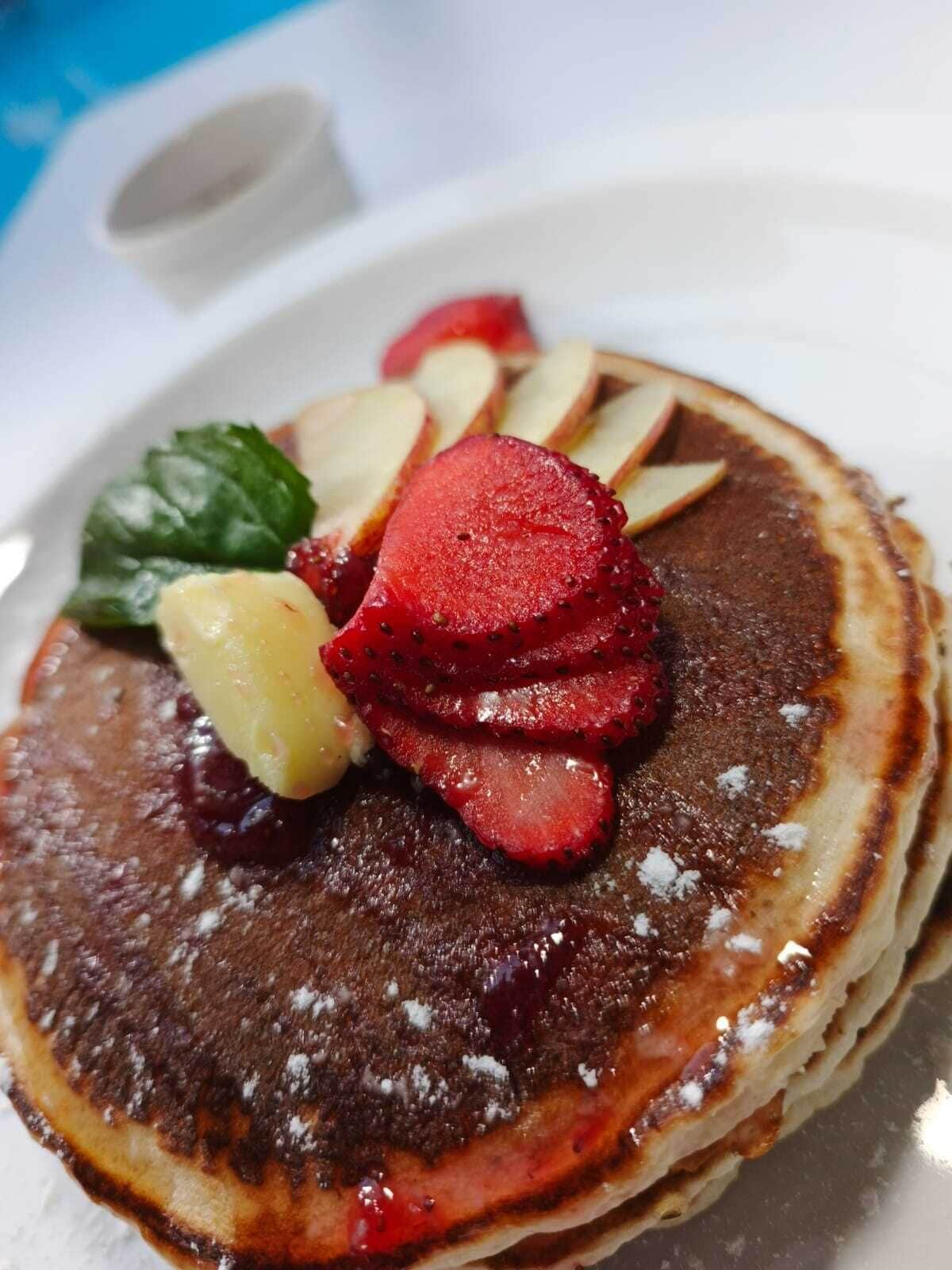 A stack of pancakes topped with strawberries, a slice of pineapple, and a mint leaf.