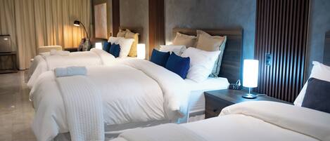 A hotel room with three beds, a nightstand with a lamp, and a large window with curtains.