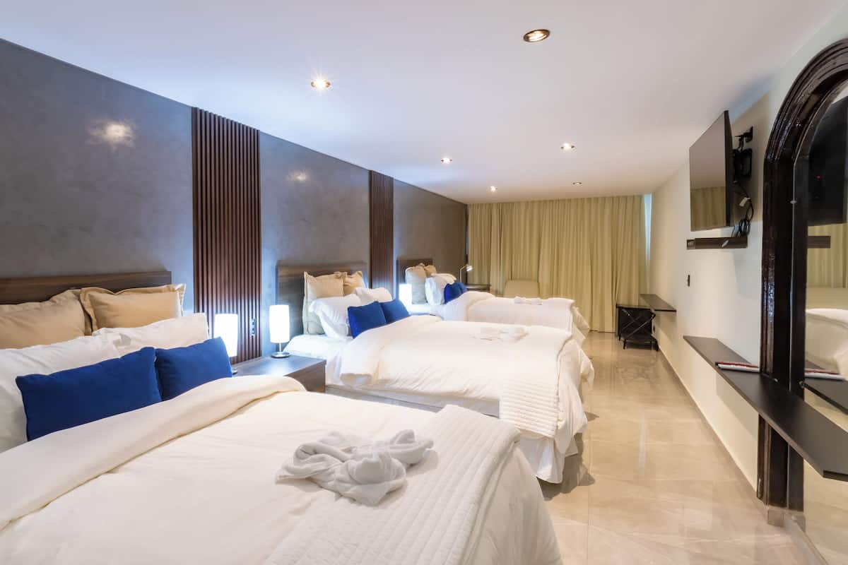 A hotel room with three beds, a large mirror, and a bathroom with a bathtub.